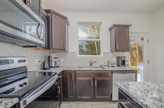 kitchen featuring dark brown cabinetry, stainless steel appliances, light stone counters, and sink