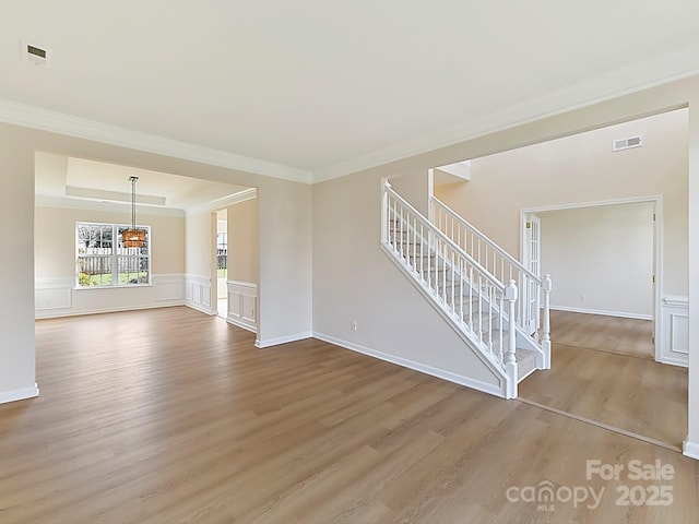 unfurnished living room featuring a raised ceiling, crown molding, and light hardwood / wood-style flooring