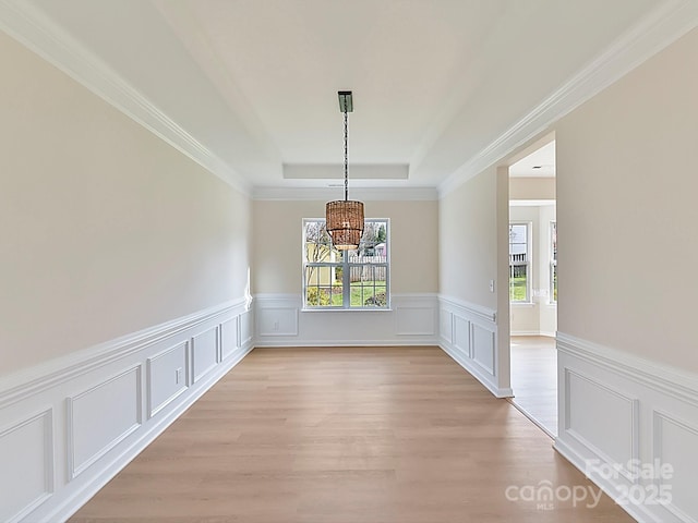 unfurnished dining area featuring a raised ceiling, light wood-type flooring, and a notable chandelier