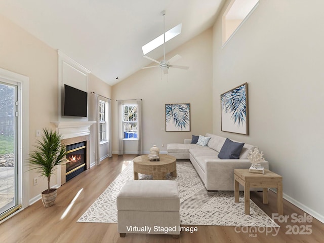 living room with vaulted ceiling with skylight, ceiling fan, and light wood-type flooring