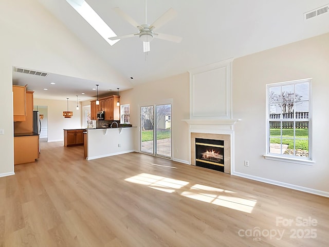 unfurnished living room with a skylight, ceiling fan, a tile fireplace, light hardwood / wood-style flooring, and high vaulted ceiling