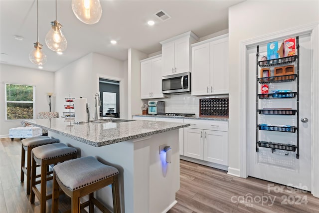 kitchen with a center island with sink, white cabinets, hanging light fixtures, light stone countertops, and light hardwood / wood-style floors