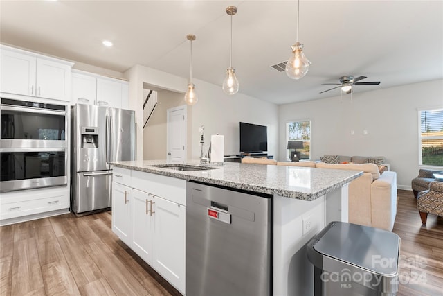 kitchen with light stone countertops, hanging light fixtures, stainless steel appliances, light hardwood / wood-style flooring, and white cabinets