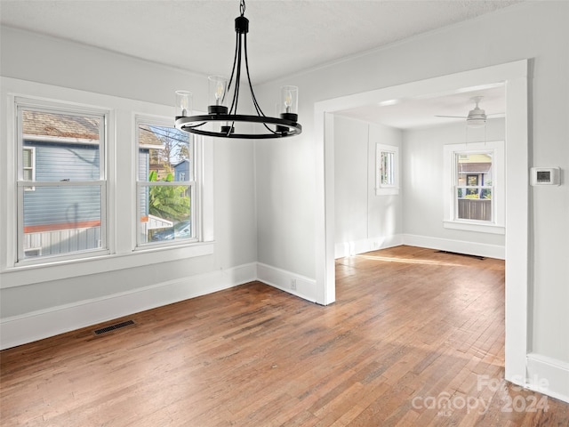 unfurnished dining area featuring hardwood / wood-style floors, a wealth of natural light, and ceiling fan with notable chandelier