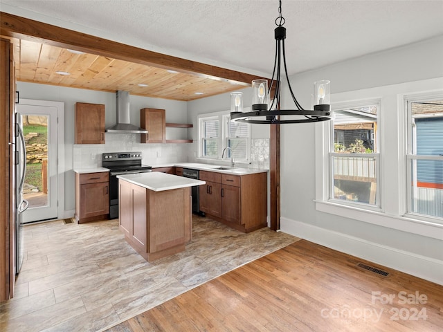 kitchen with light hardwood / wood-style floors, appliances with stainless steel finishes, an inviting chandelier, a center island, and wall chimney range hood