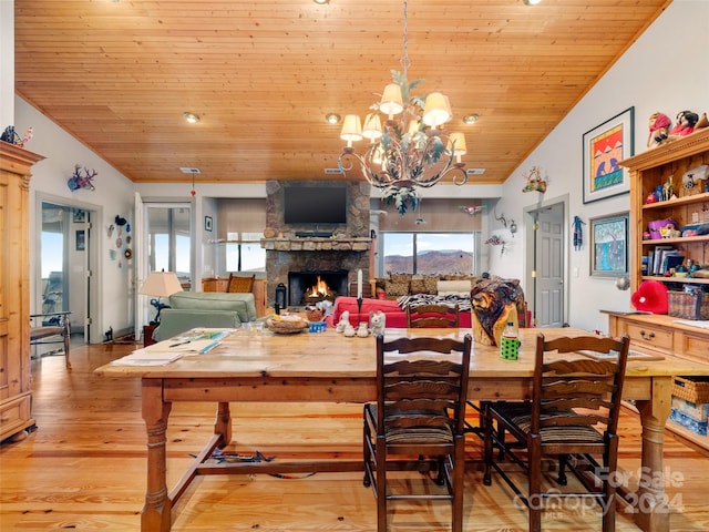 dining area featuring a stone fireplace, an inviting chandelier, vaulted ceiling, wooden ceiling, and light hardwood / wood-style flooring