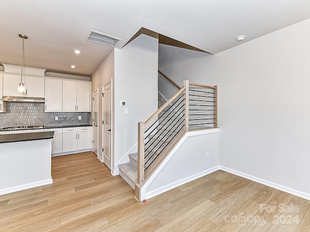 kitchen featuring tasteful backsplash, pendant lighting, light hardwood / wood-style flooring, white cabinetry, and stainless steel gas stovetop