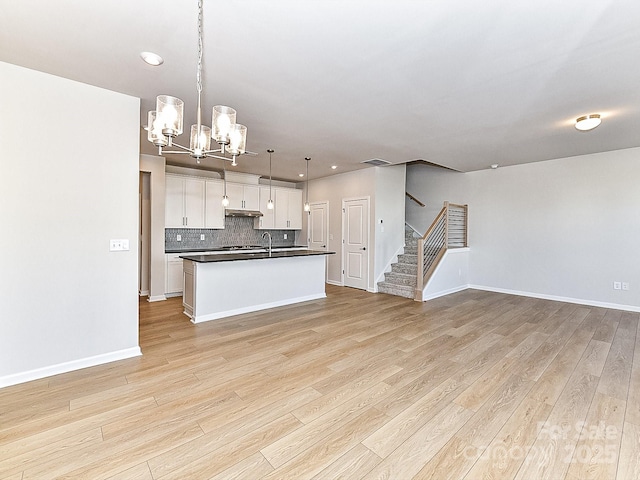 kitchen with backsplash, a kitchen island with sink, a notable chandelier, white cabinets, and hanging light fixtures