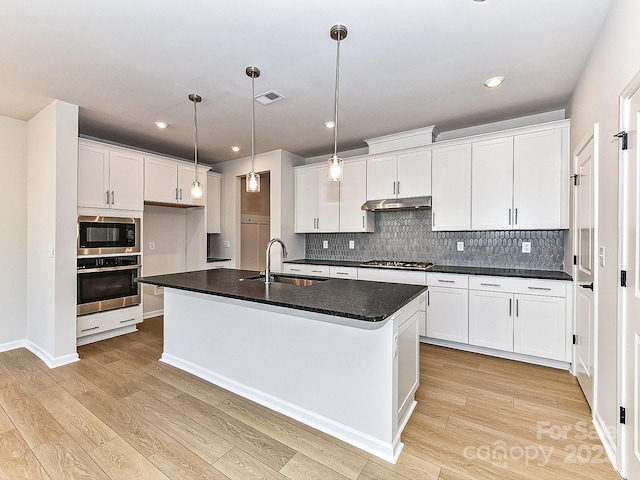 kitchen featuring white cabinets, sink, an island with sink, decorative light fixtures, and stainless steel appliances