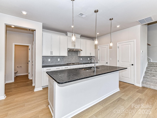 kitchen featuring white cabinets, a center island with sink, sink, hanging light fixtures, and decorative backsplash