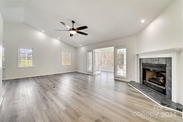 unfurnished living room with high vaulted ceiling, ceiling fan, a tiled fireplace, and light hardwood / wood-style floors