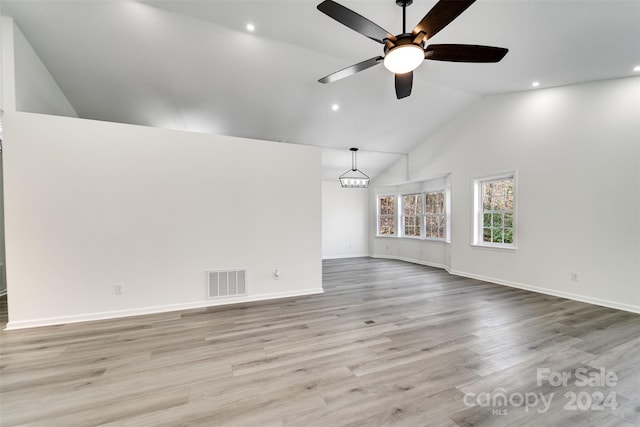 unfurnished living room featuring ceiling fan with notable chandelier, light hardwood / wood-style floors, and high vaulted ceiling