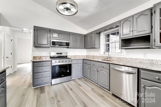 kitchen with light hardwood / wood-style flooring, sink, appliances with stainless steel finishes, lofted ceiling, and gray cabinets