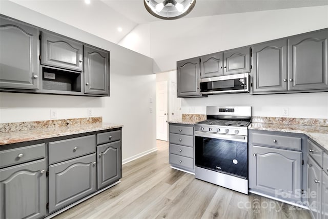 kitchen with light hardwood / wood-style flooring, high vaulted ceiling, gray cabinets, stainless steel appliances, and light stone counters