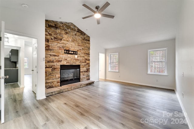 unfurnished living room with a stone fireplace, ceiling fan, lofted ceiling, and light wood-type flooring