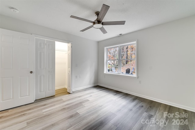 unfurnished bedroom with a closet, a textured ceiling, light hardwood / wood-style floors, and ceiling fan