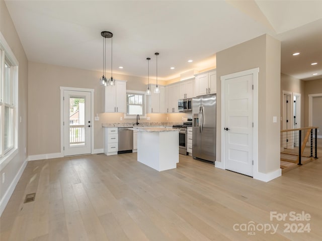 kitchen with white cabinetry, appliances with stainless steel finishes, pendant lighting, light hardwood / wood-style floors, and a center island