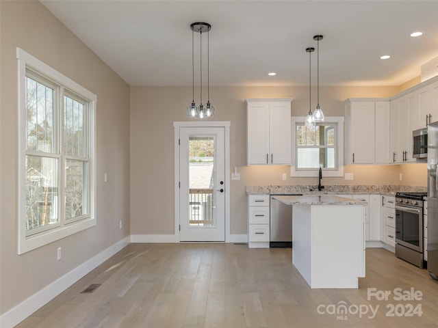 kitchen with white cabinets, decorative light fixtures, light hardwood / wood-style floors, and stainless steel appliances