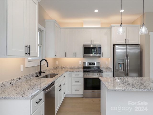 kitchen featuring sink, white cabinetry, light wood-type flooring, appliances with stainless steel finishes, and decorative light fixtures