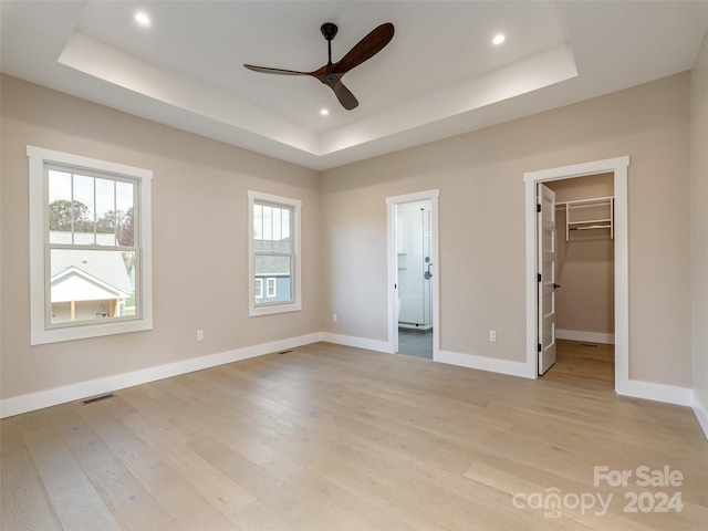 unfurnished bedroom featuring a tray ceiling, a spacious closet, ceiling fan, and light hardwood / wood-style flooring