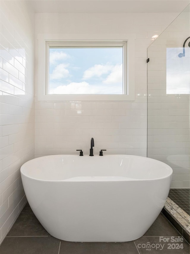 bathroom featuring tile walls, tile patterned flooring, a bathtub, and a healthy amount of sunlight