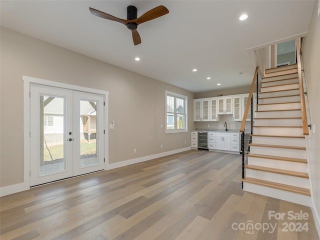 unfurnished living room featuring ceiling fan, beverage cooler, light hardwood / wood-style flooring, and french doors