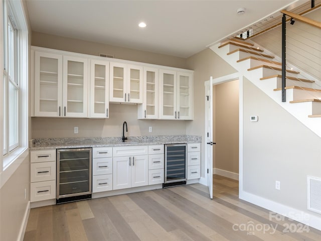 kitchen featuring white cabinets, light stone countertops, light hardwood / wood-style flooring, and wine cooler