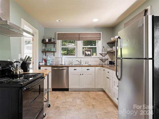 kitchen with butcher block counters, white cabinetry, sink, appliances with stainless steel finishes, and wall chimney range hood