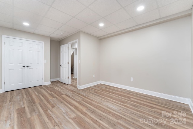 unfurnished bedroom with a paneled ceiling, light hardwood / wood-style flooring, and a closet