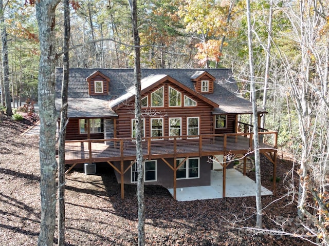 rear view of property featuring roof with shingles, central AC unit, log exterior, a deck, and a patio