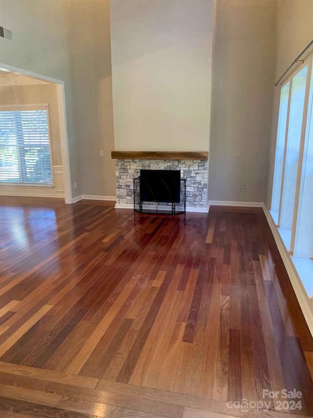 unfurnished living room featuring a fireplace, dark wood-type flooring, and a high ceiling