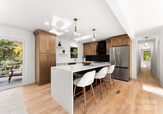 kitchen featuring stainless steel appliances, custom exhaust hood, decorative light fixtures, light hardwood / wood-style flooring, and a center island