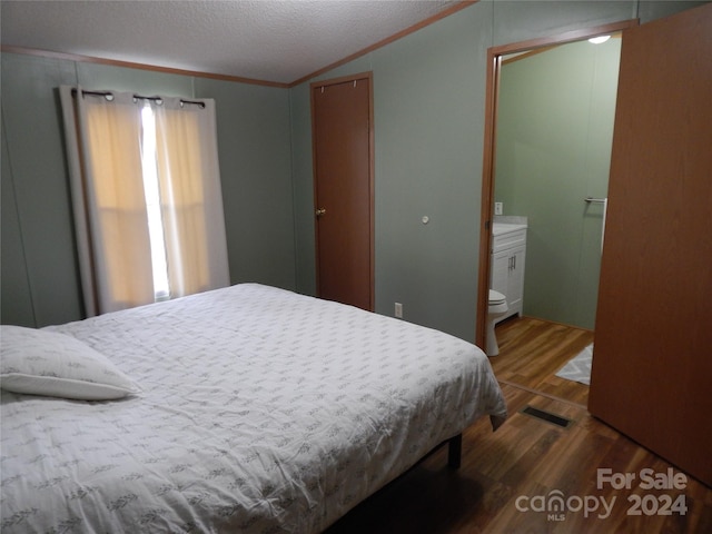 bedroom with ornamental molding, hardwood / wood-style floors, ensuite bath, and a textured ceiling