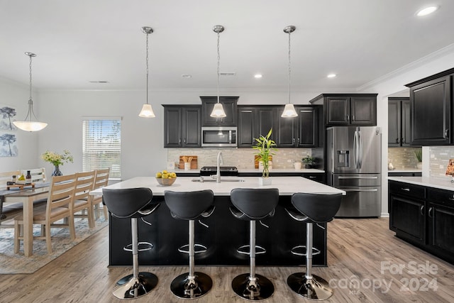 kitchen featuring a kitchen island with sink, hanging light fixtures, stainless steel appliances, and light hardwood / wood-style floors