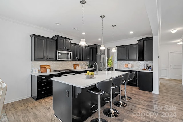 kitchen with a kitchen island with sink, light wood-type flooring, appliances with stainless steel finishes, decorative light fixtures, and a breakfast bar area