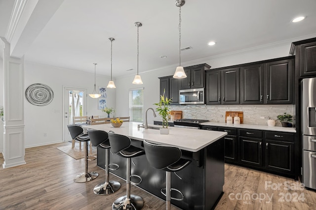 kitchen featuring a center island with sink, pendant lighting, light wood-type flooring, and appliances with stainless steel finishes