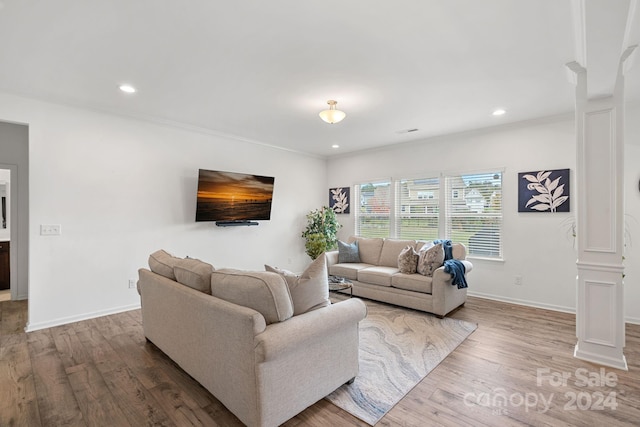 living room featuring wood-type flooring, ornamental molding, and decorative columns