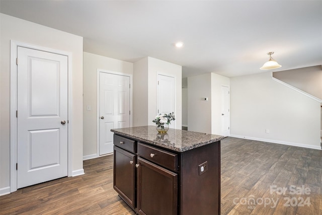 kitchen featuring dark hardwood / wood-style floors, a kitchen island, light stone counters, and decorative light fixtures