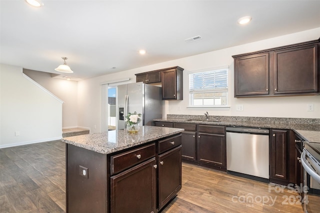 kitchen with a center island, sink, hardwood / wood-style flooring, stone countertops, and stainless steel appliances