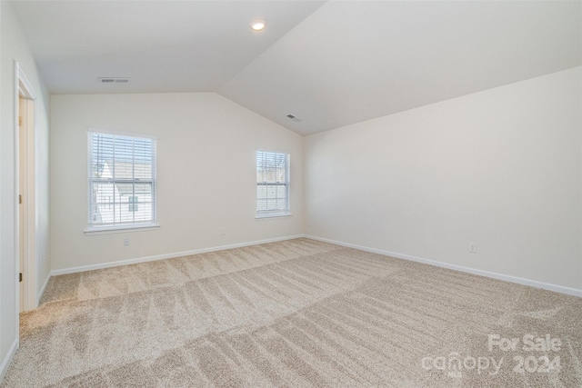 spare room featuring a healthy amount of sunlight, light carpet, and vaulted ceiling