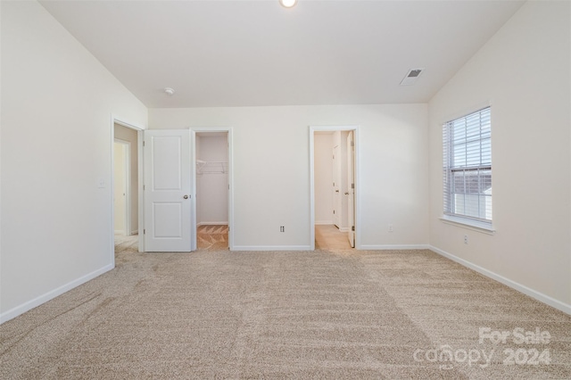 unfurnished bedroom featuring a walk in closet, light colored carpet, a closet, and lofted ceiling