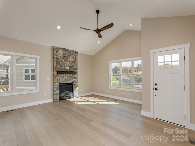 unfurnished living room with a stone fireplace, light wood-type flooring, a wealth of natural light, and ceiling fan