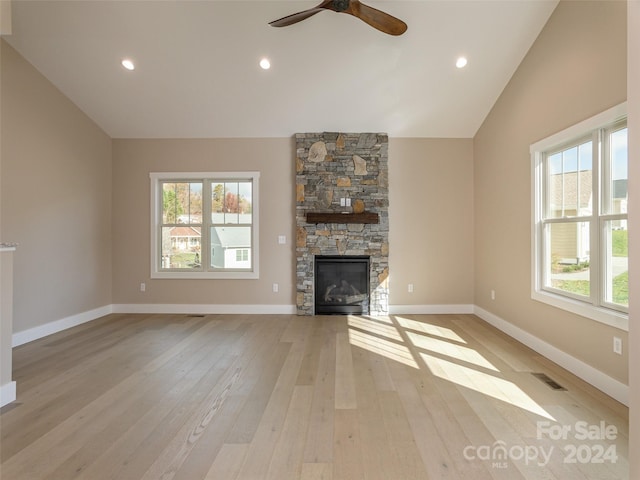 unfurnished living room with a stone fireplace, light hardwood / wood-style flooring, lofted ceiling, and ceiling fan