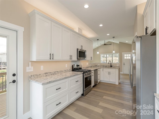 kitchen featuring stainless steel appliances, hanging light fixtures, vaulted ceiling, white cabinets, and light hardwood / wood-style flooring