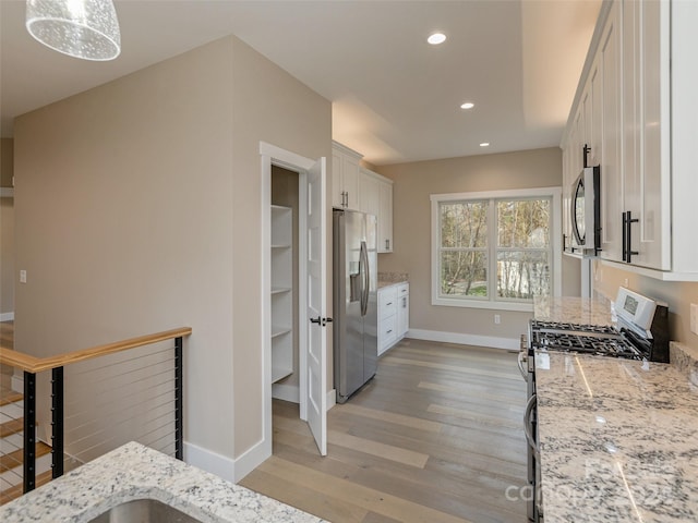 kitchen featuring stainless steel appliances, light stone countertops, decorative light fixtures, white cabinets, and light wood-type flooring