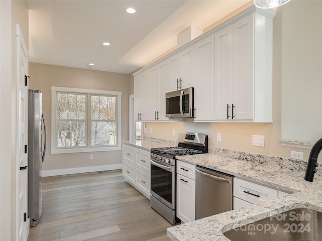 kitchen featuring white cabinets, sink, light stone countertops, light wood-type flooring, and appliances with stainless steel finishes