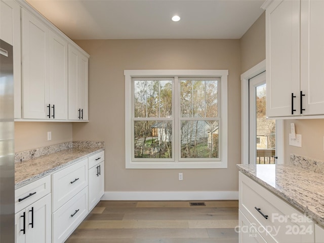 kitchen with white cabinetry, light stone counters, and light hardwood / wood-style floors