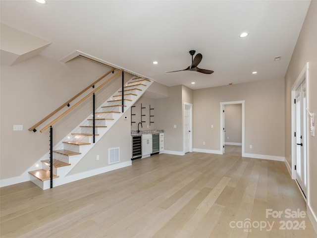 unfurnished living room featuring light hardwood / wood-style floors, ceiling fan, wine cooler, and wet bar