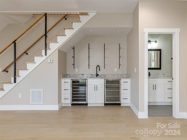 bar with light stone countertops, light wood-type flooring, and wine cooler