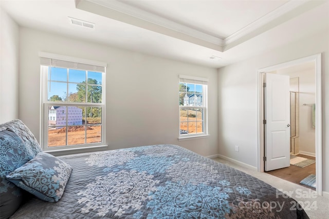 carpeted bedroom featuring a tray ceiling, crown molding, and ensuite bathroom